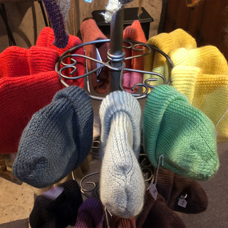 A display of multiple hand-knit beret hats in various colors, including red, yellow, green, blue, white, brown, and purple, arranged on a metal stand.
