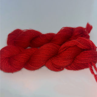 Two braided skeins of vibrant red  yarn on a plain light background.