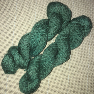 Two twisted hanks of dark green yarn laid on a beige woven fabric background.