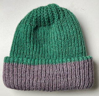 A hand-made knit beanie hat with a two-tone design, featuring a vibrant green upper section and a muted purple-gray folded cuff, shown against a plain off-white background.
