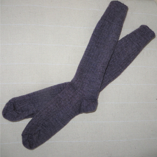 A pair of dark purple ribbed knit socks laid flat on a light beige textured fabric background.