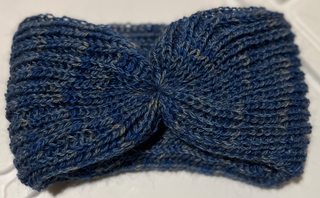 A handmade, hand-knotted headband in a heathered blue and gray yarn, displayed on a plain white surface.