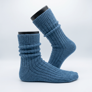 A pair of ribbed knit crew socks in a dusty medium blue color, displayed on black mannequin feet against a clean white studio background.