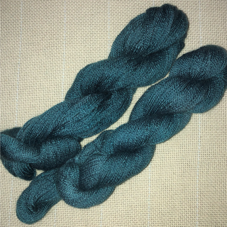 Two twisted skeins of dark teal blue yarn laid flat on a light beige textured fabric background.
