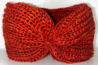A handmade, knit headband in a cherry red  yarn, styled in a bow shape against a plain white background.