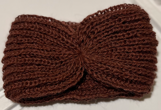 A brown knitted headband with a twisted front detail, laid flat on a white textured surface.