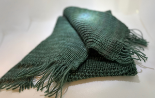 A folded dark green knitted scarf with fringed edges, displayed on a plain white surface.