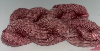 A twisted skein of dusty rose pink yarn on a plain white background.