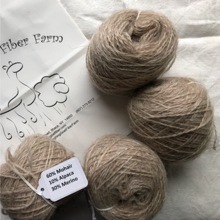 Four balls of natural beige mohair yarn arranged on a white fabric background next to a branded Fiber Farm paper bag. A white product tag is attached to one ball showing the blend: 60% Mohair, 10% Alpaca, 30% Merino.