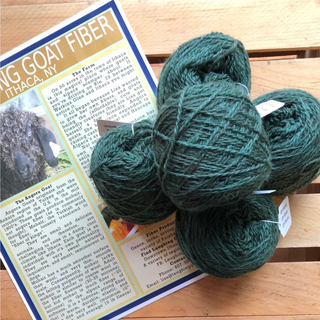 Four skeins of dark green wool yarn arranged on top of a printed informational card about goat fiber, placed on a wooden surface.