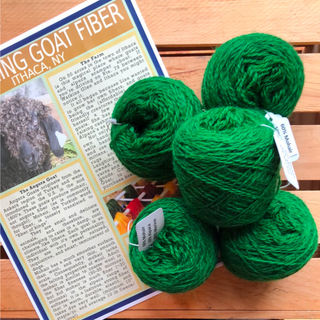 Four bright green ball of yarn arranged on a wooden slatted surface next to a printed informational card about goat fiber.