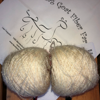Two balls of cream-colored MOHAIR yarn placed on top of a white paper label printed with 'Laughing Goat Fiber Farm'.