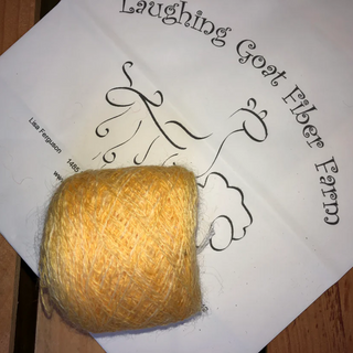 A ball of soft yellow yarn placed on a white paper label printed with the text 'Laughing Goat Fiber Farm'.