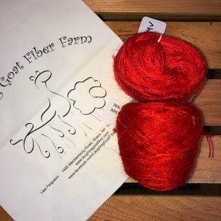 Two balls of variegated red yarn placed on a wooden slatted surface next to a printed card from Goat Fiber Farm.