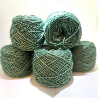 Five balls of dusty sage green yarn stacked together on a plain white background.