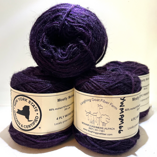 Four skeins of deep purple yarn stacked together, showing cream paper labels with text including 'Laughing Goat Fiber Farm' and '4 Ply Worsted'.