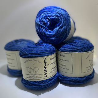 Four balls of blue yarn stacked together on a light gray background, with paper labels showing the brand Laughing Goat Fiber Farm and product details.