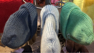 A display of multiple knit beret hats in various colors, including red, yellow, green, blue, white, brown, and purple, arranged on a metal stand.