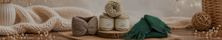 A styled flat-lay of knitted and crocheted textile items on a wooden surface, including cream-colored chunky knit blankets, a beige knitted hat, two cream yarn balls, a dark green knitted scarf, and a woven ball, with warm bokeh lights in the background.